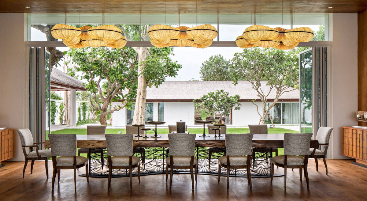 Modern dining room with large windows overlooking a garden and contemporary lighting fixtures.
