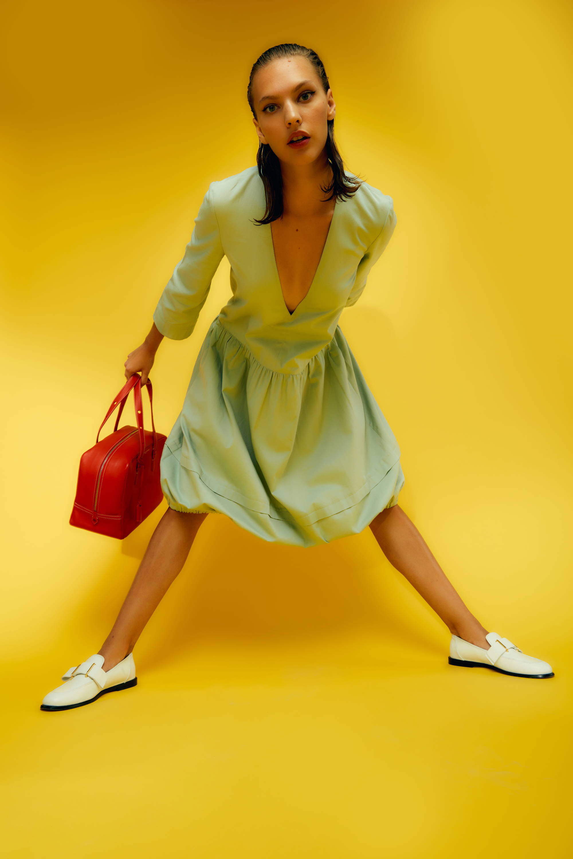 Model in a blue dress poses with a red bag against a yellow background.