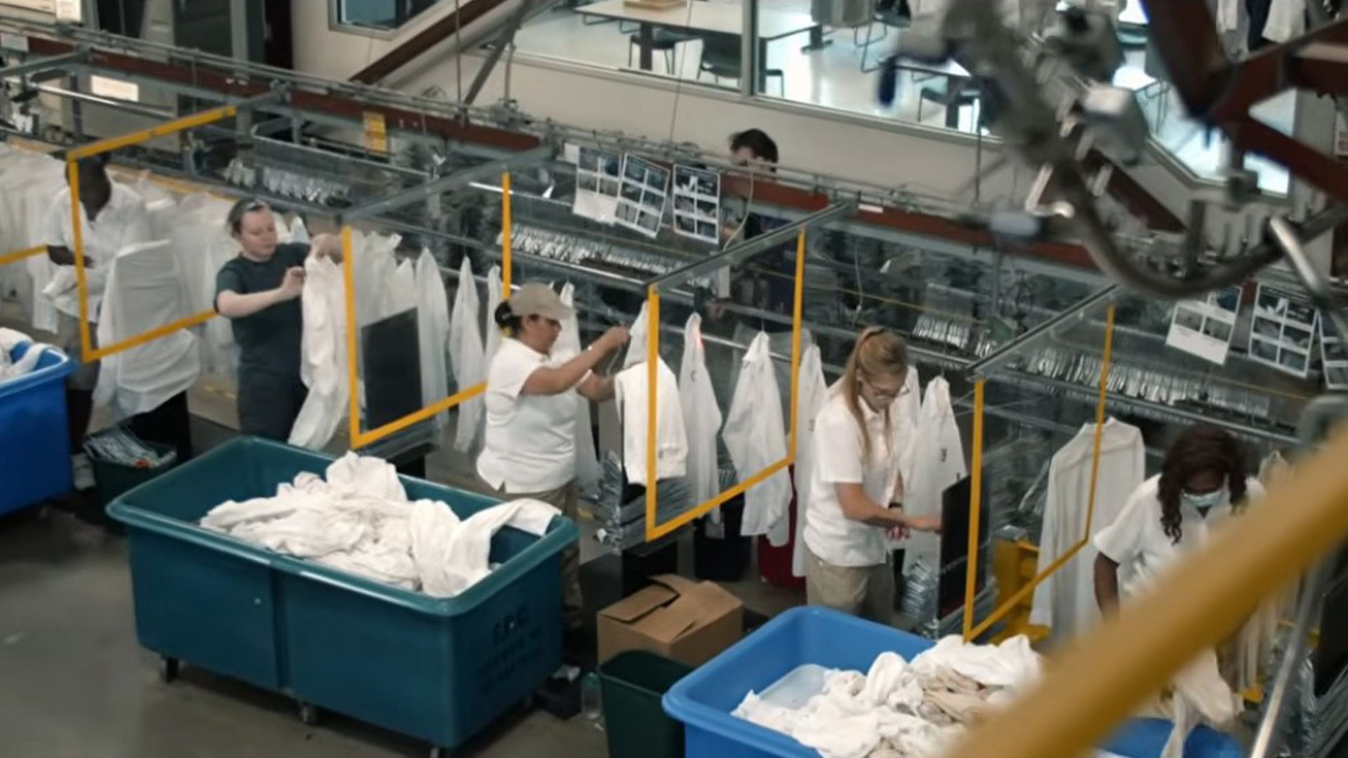 Workers sorting and hanging white garments in a laundry facility.
