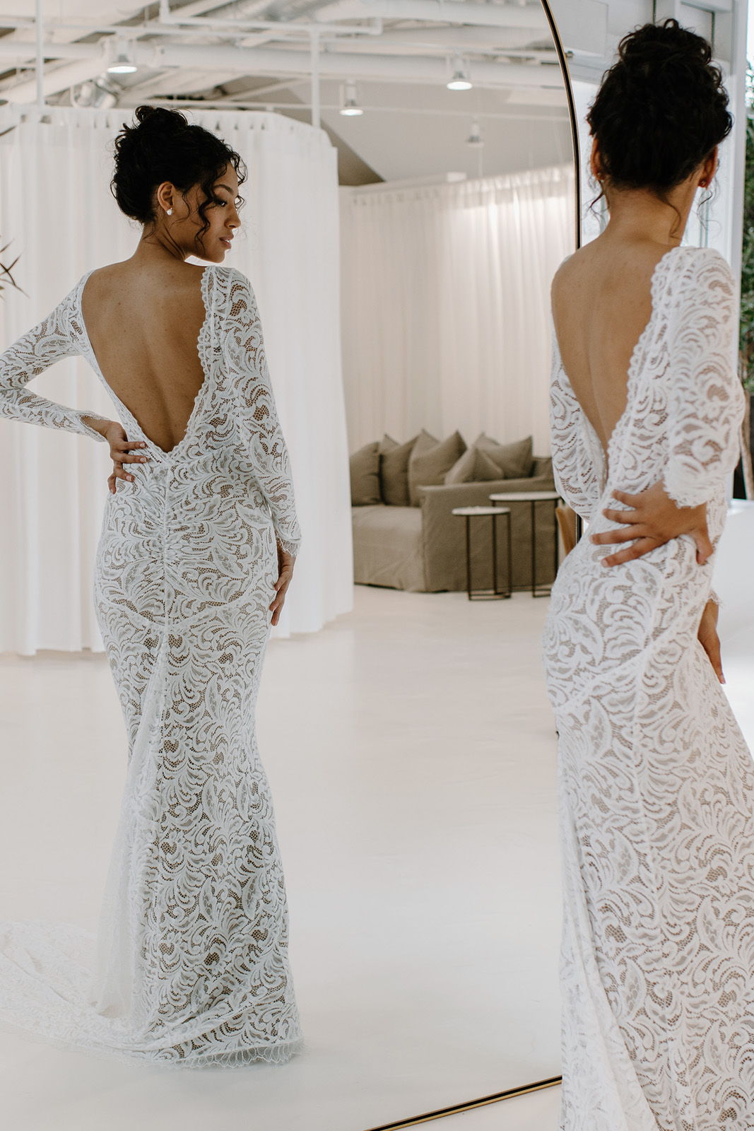 A woman in a lace dress poses in front of a mirror.