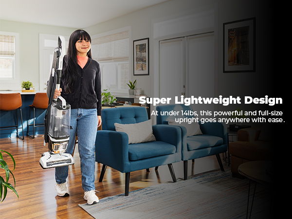 A woman carrying a vacuum in a modern living room.