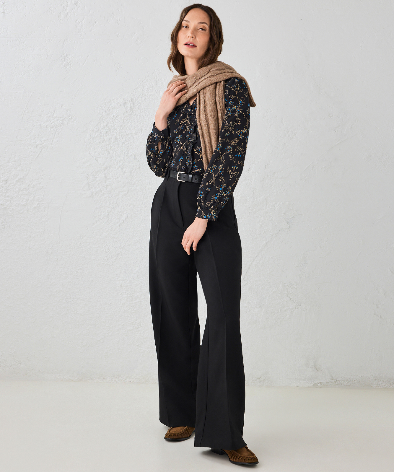 Woman in a patterned blouse and wide-leg pants, holding a scarf.