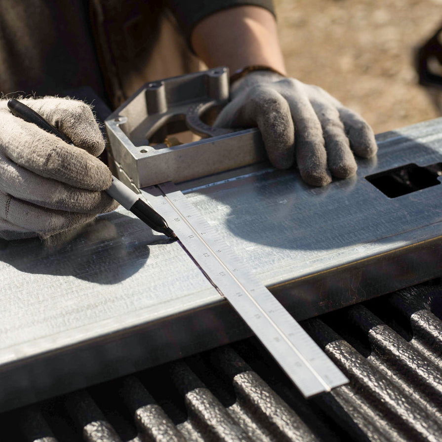 Person marking metal with a square tool on a work surface.
