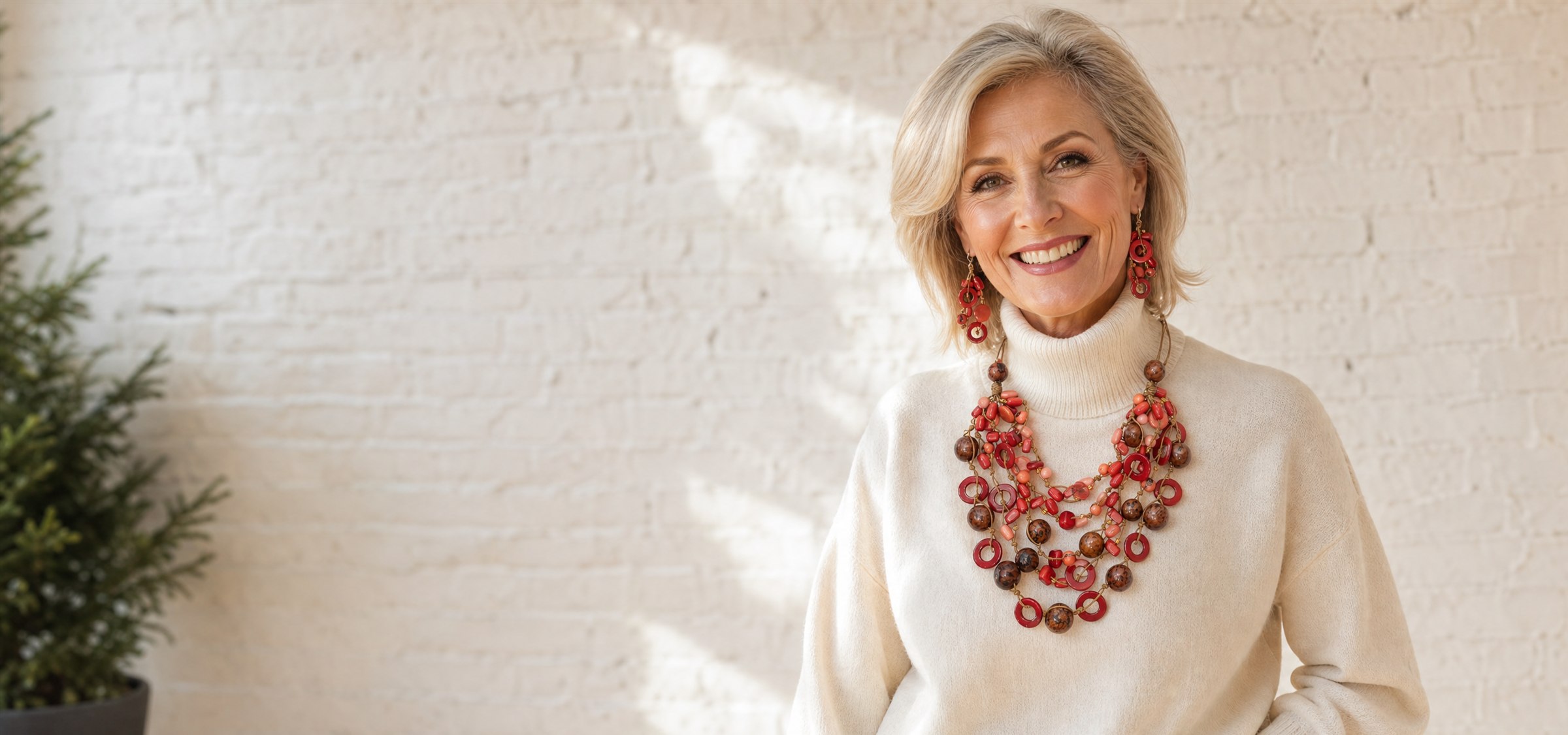 Smiling woman in a cream turtleneck wearing a layered red tagua statement necklace and matching earrings