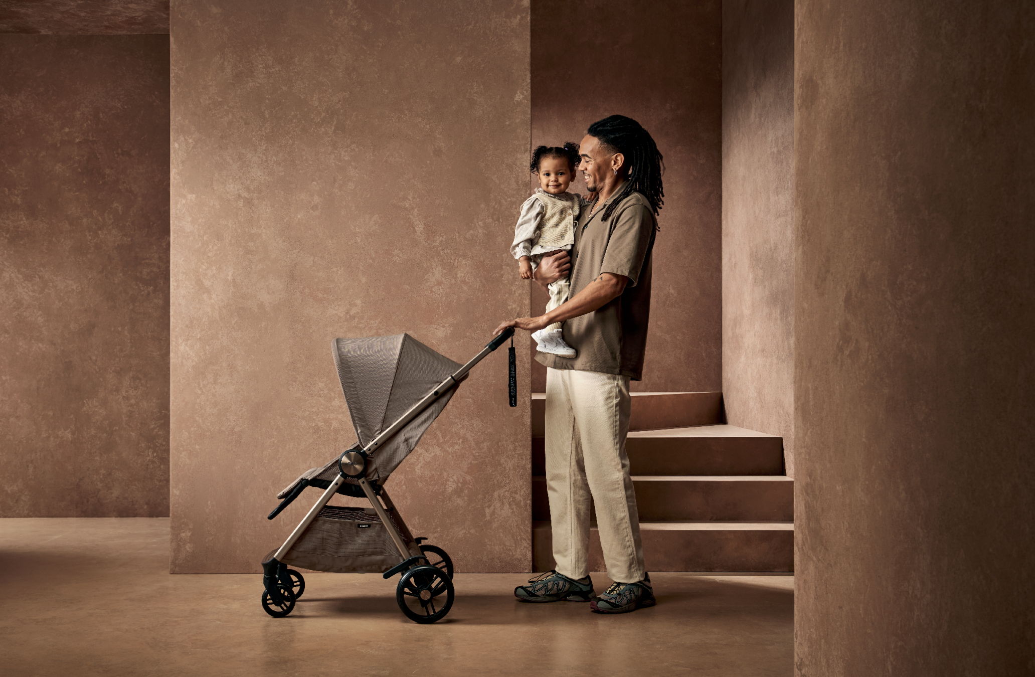 Person holding a child near a stroller in a minimalist interior.