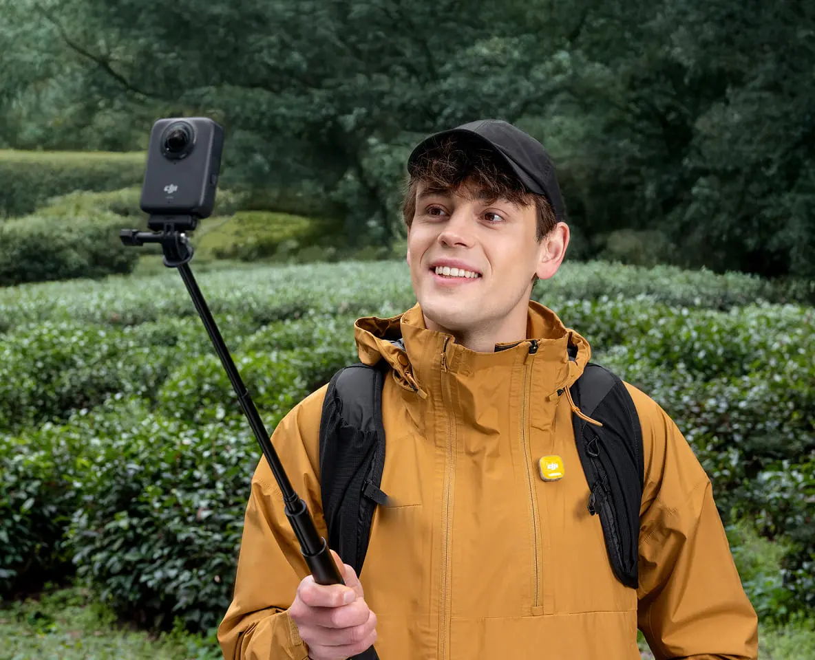 Person in a yellow jacket taking a selfie with a DJI Osmo 360 camera on a stick.