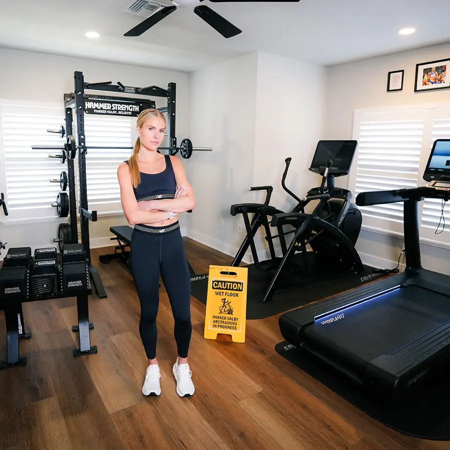 Woman standing in a gym with exercise equipment and a caution sign.