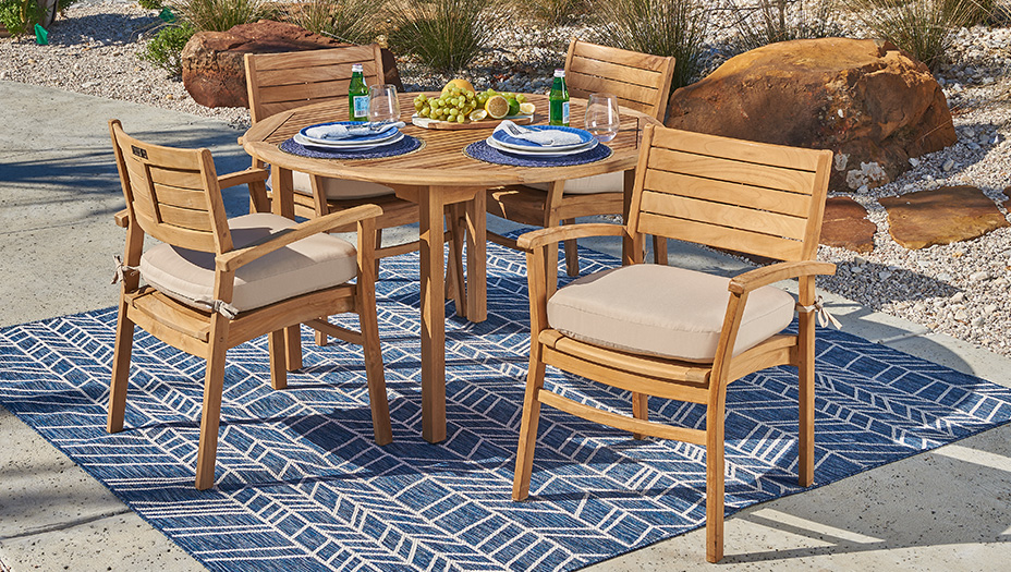 Outdoor dining set with wooden table and chairs on a patterned rug.
