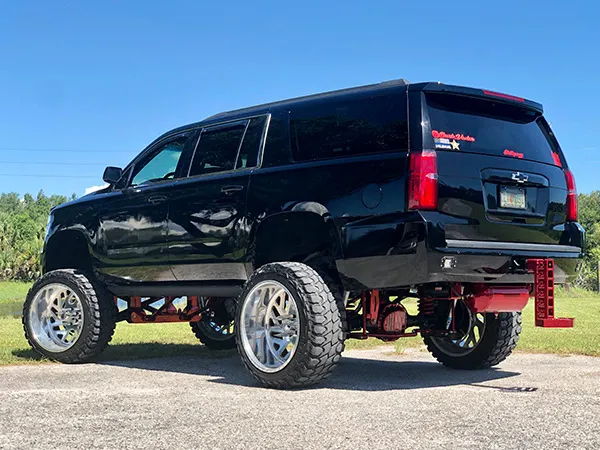 Rear three-quarter view of Corey's lifted black 2018 Chevrolet Suburban with custom wheels and red suspension, install photo 3