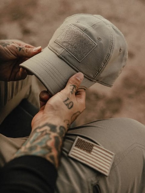 Person holding a gray hat, showing tattoos and an American flag patch.