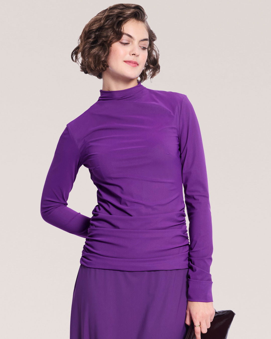 Woman wearing a purple long-sleeve top, smiling against a neutral background.