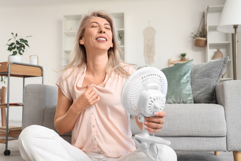 Woman sitting on the floor, using a fan, looking relieved and happy.