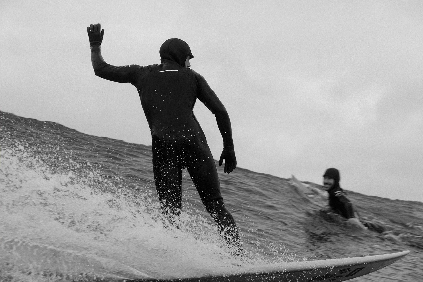 Two surfers riding waves in black and white.