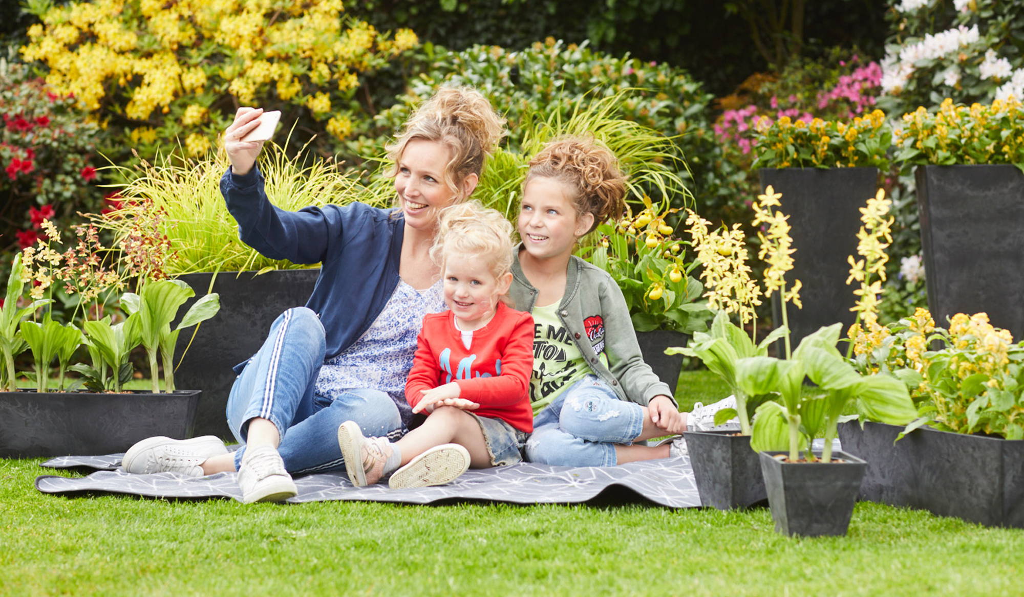 Mother and daughters taking a selfie while sitting outside next to their potted plants
