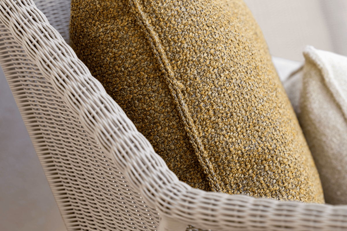 Close-up of a textured yellow outdoor throw pillow on a light woven outdoor chair.