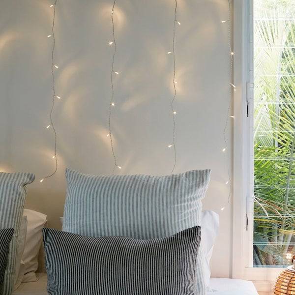 Warm white curtain lights on a wall behind a bed.