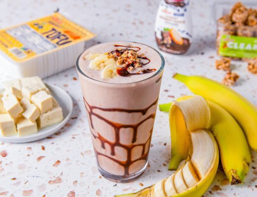 A glass of chocolate smoothie with bananas and toppings on a countertop.