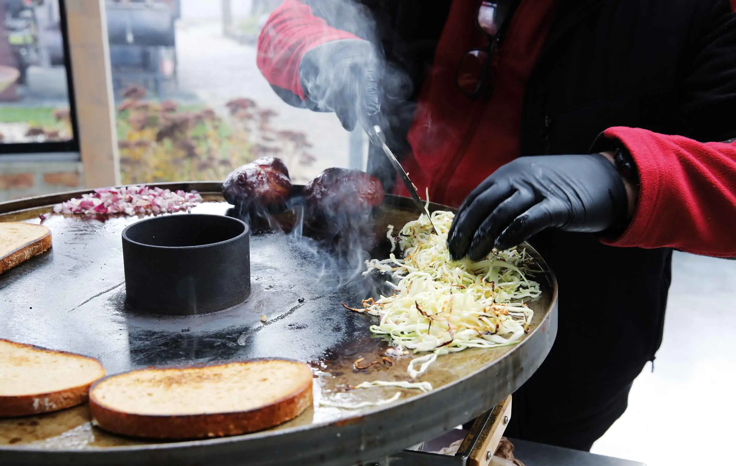 Person cooking on a grill, chopping ingredients with smoke rising.