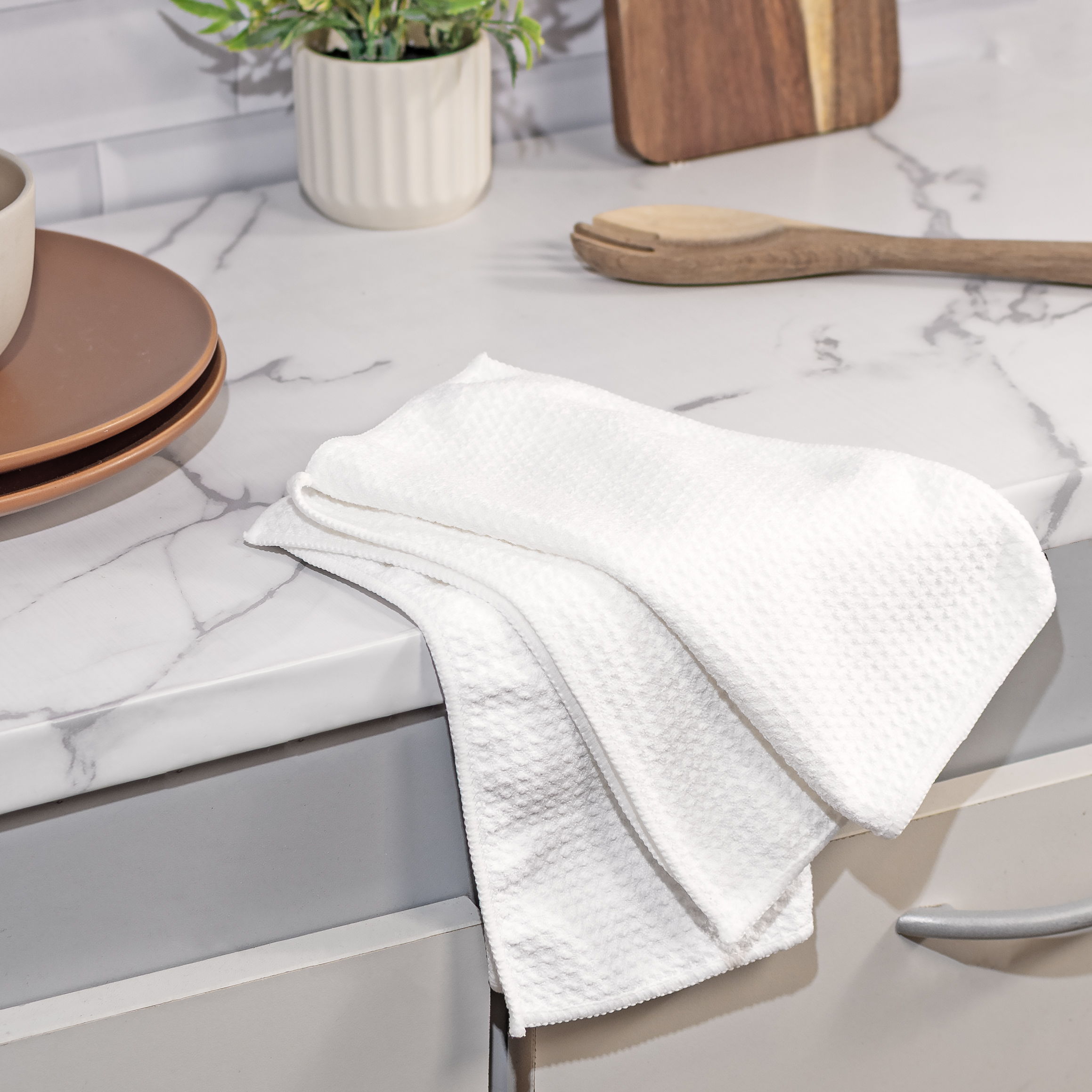 White kitchen towels neatly placed on a marble countertop with utensils.