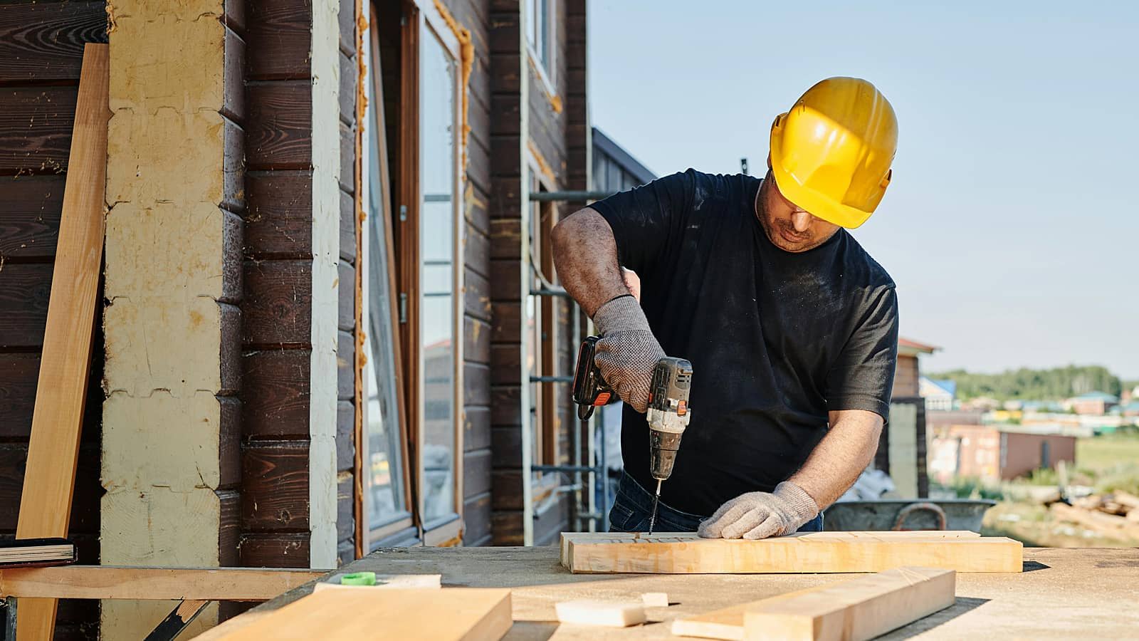 Construction worker using a drill on wooden boards outdoors.