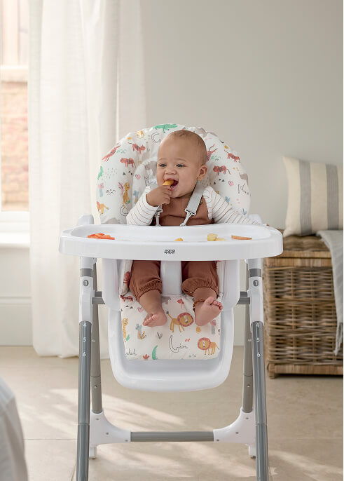 Baby sitting in a Snax Highchair - Jungle Alphabet, enjoying a snack in a bright room.