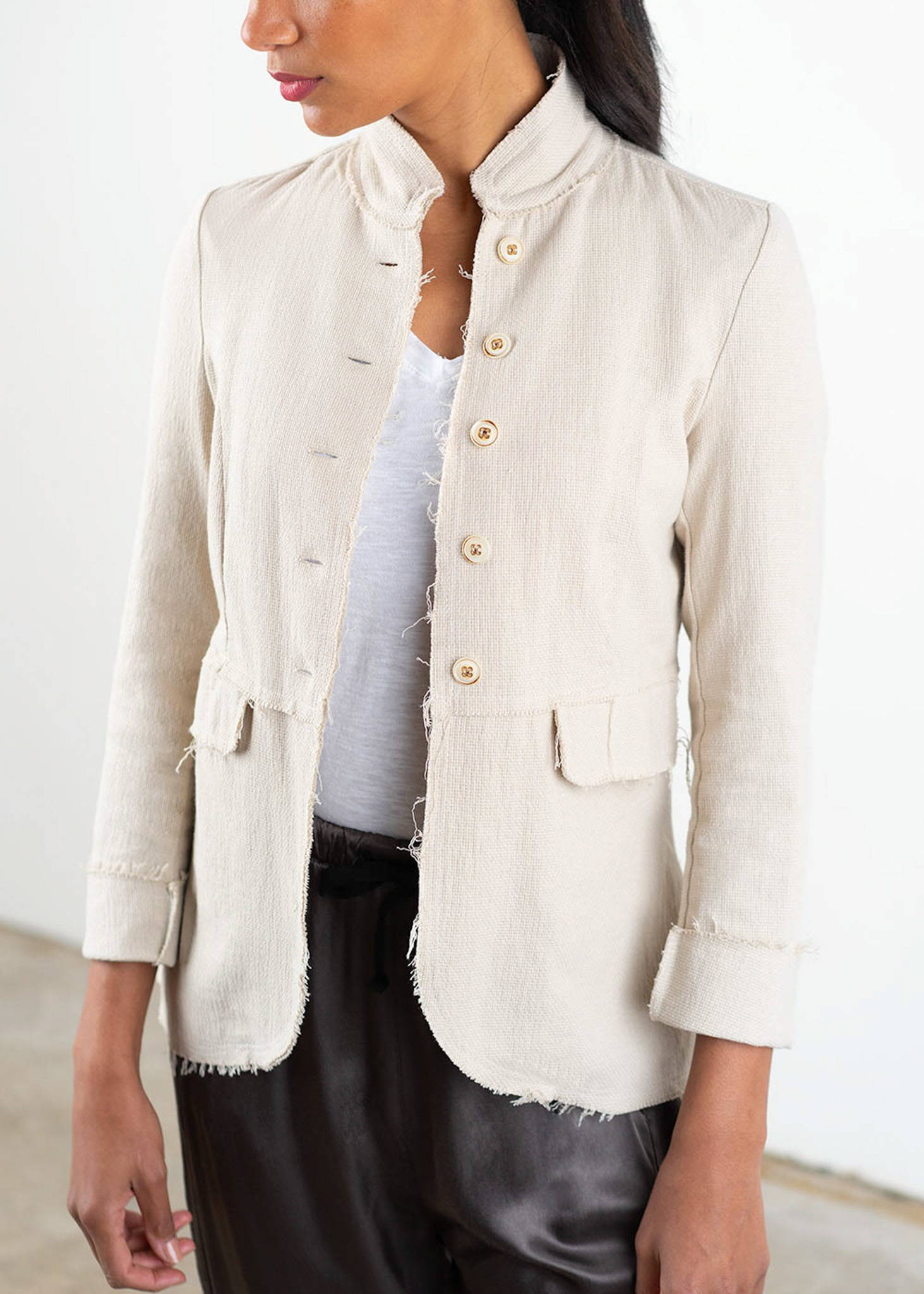 A model wearing a white cotton mix jacket with raw hem detailing over a white top and dark grey trousers