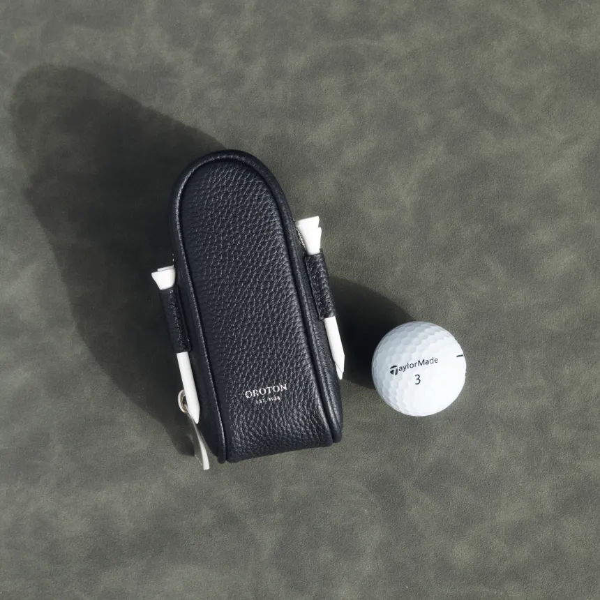 Black textured bag next to a white round object on a gray surface.