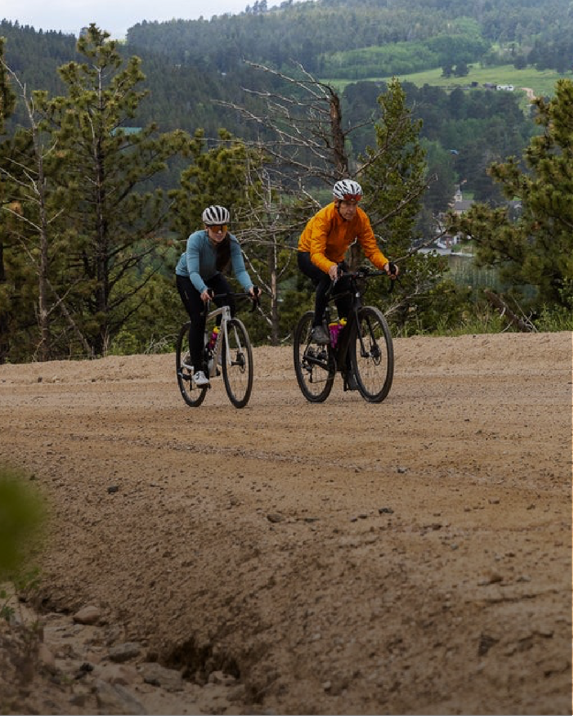 Male and female cyclists riding uphill on a gravel road wearing long sleeve PEARL iZUMi cycling gear.
