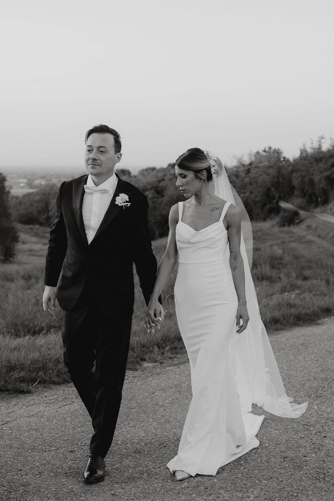 Bride and groom walking hand in hand along a scenic path.