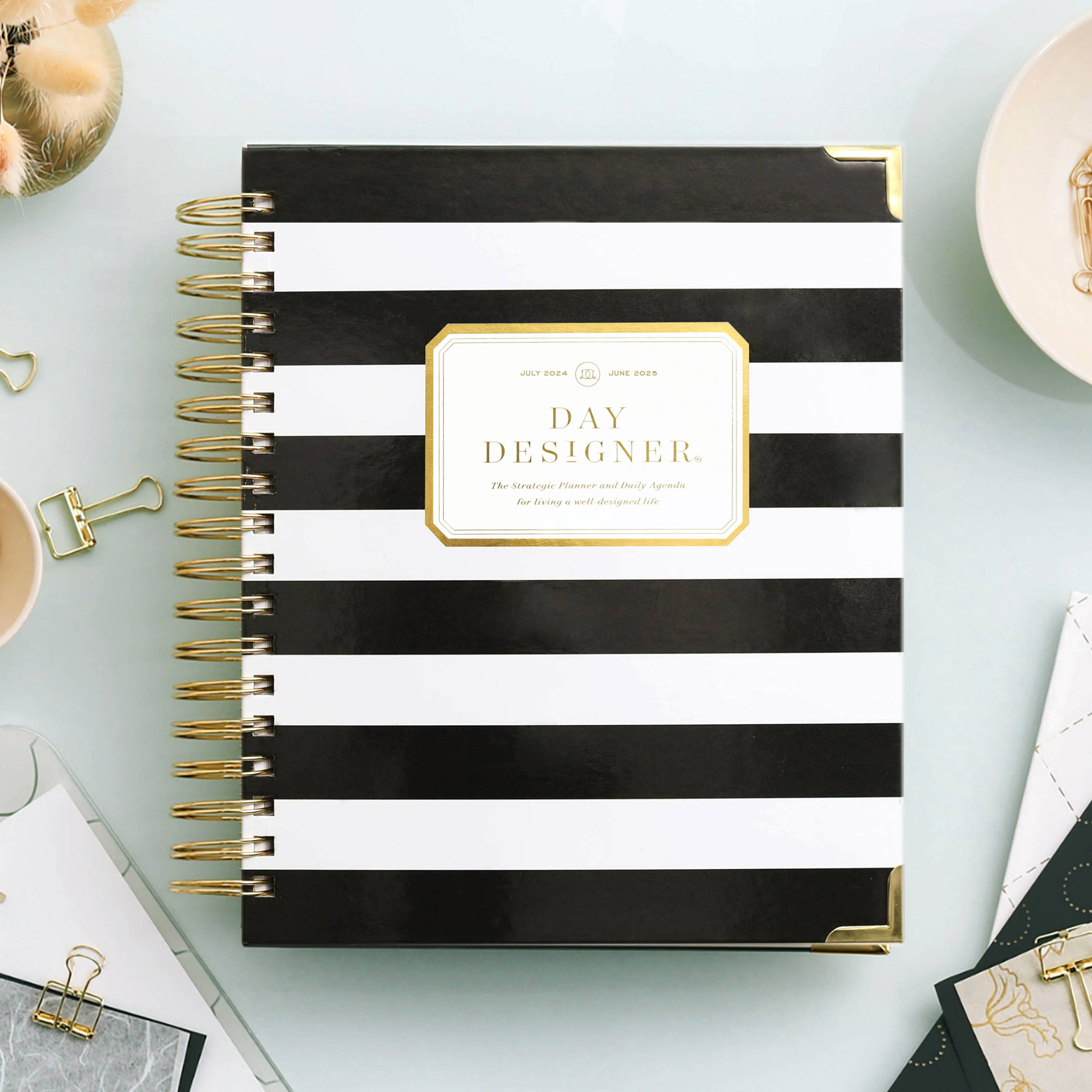 black and white stripe closed book planner on mint green background, paper clips, paper, dish and dried flowers