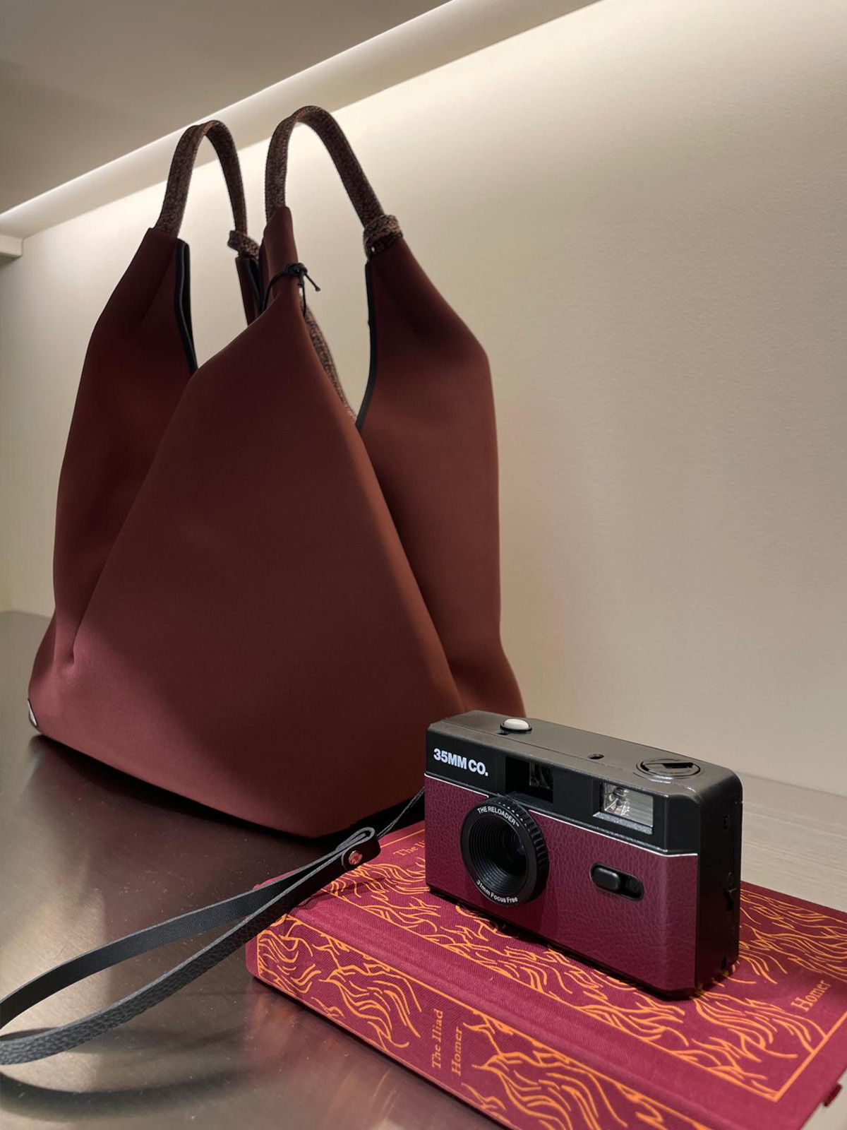 A brown tote bag, a camera, and a notebook on a table.