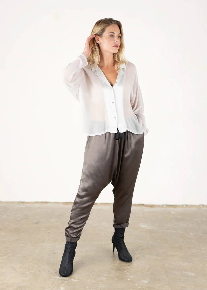A model wearing a pair of dark grey satin trousers with black heels and an off white long sleeved shirt blouse