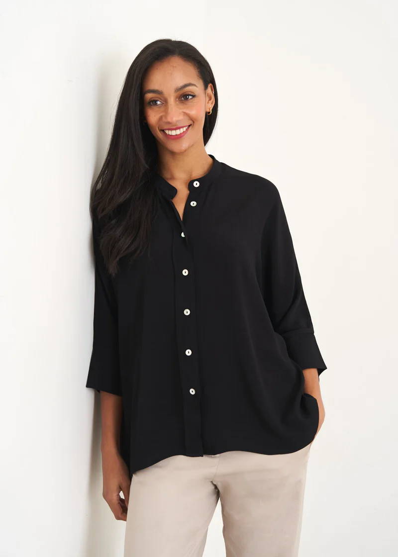 A model wering a relaxed overszied black button down shirt with off white trousers and 3/4 sleeves