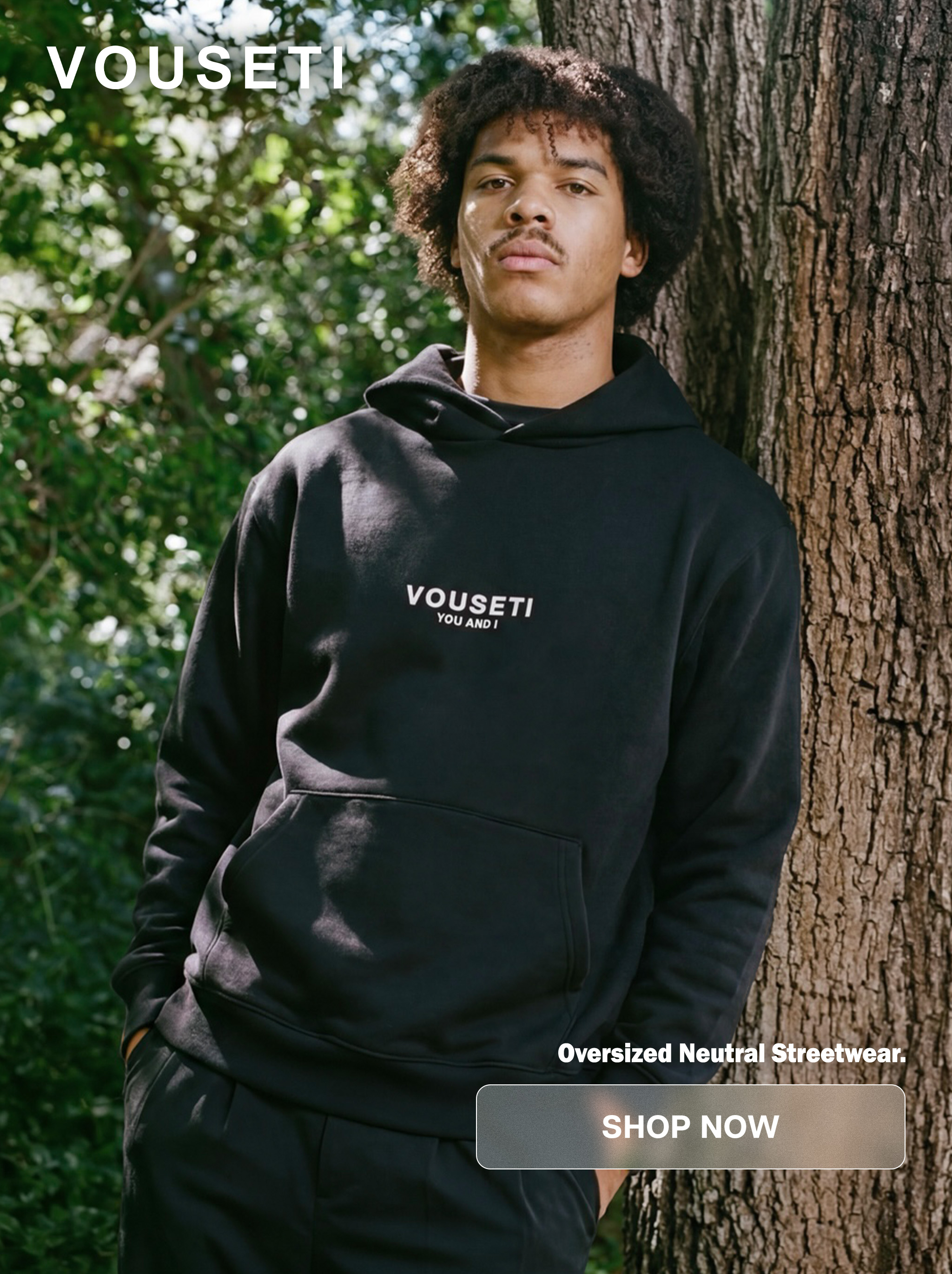 A person in a black hoodie stands beside a tree.
