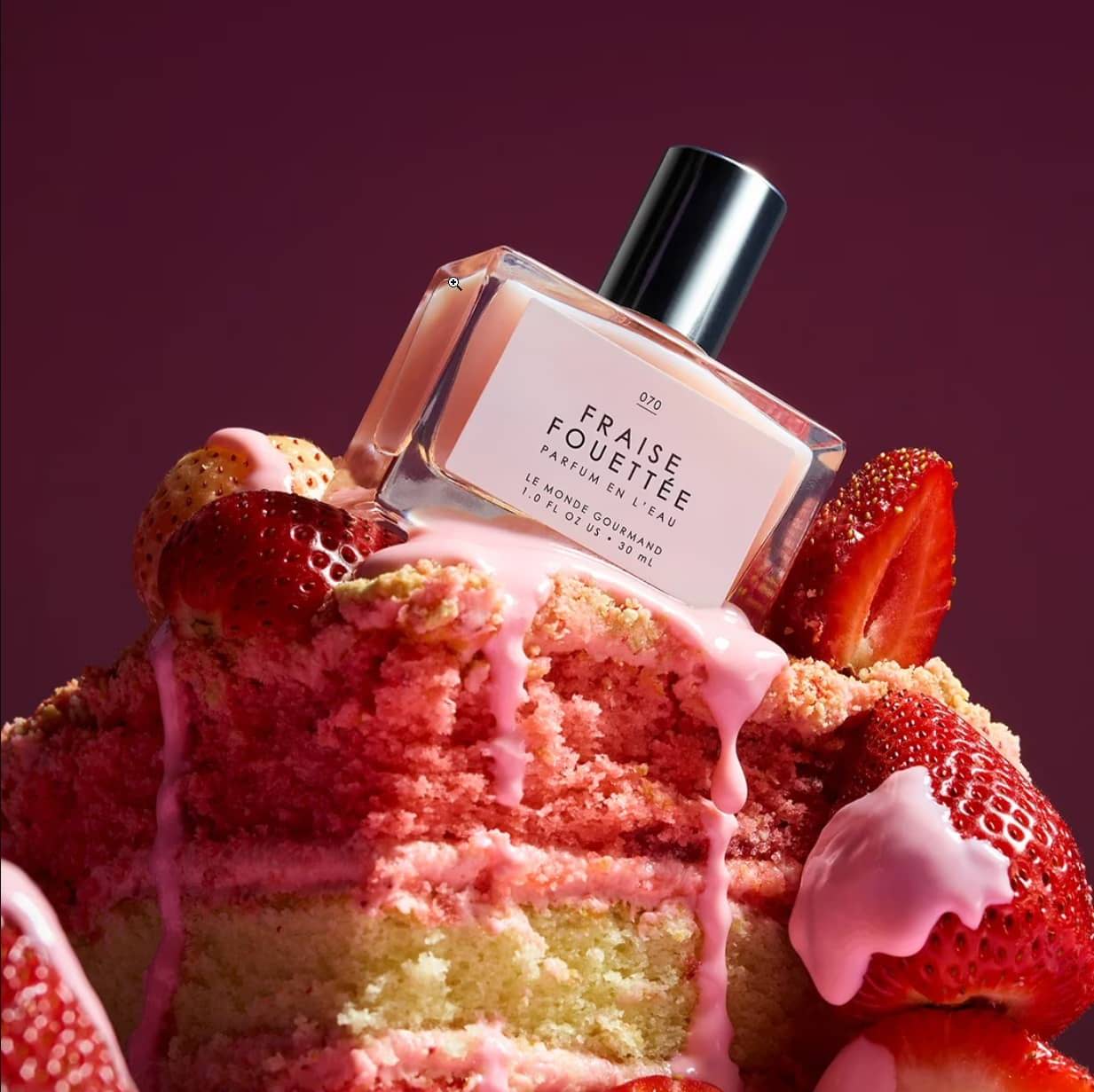 Perfume bottle placed on a colorful cake with strawberries and icing.