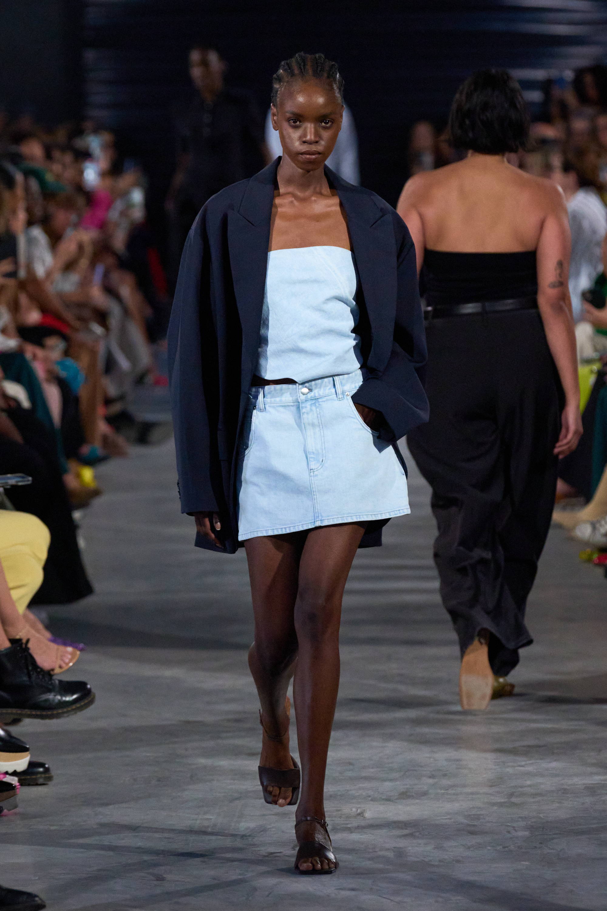 Model on a runway wearing denim top and skirt with blazer