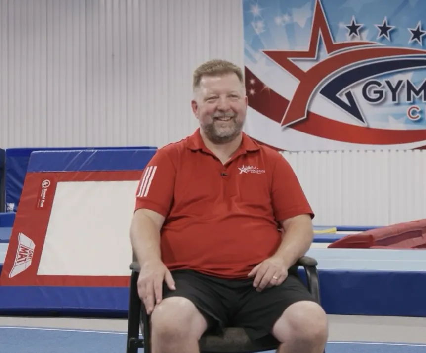 Smiling man in a wheelchair sitting in a gymnastics gym.