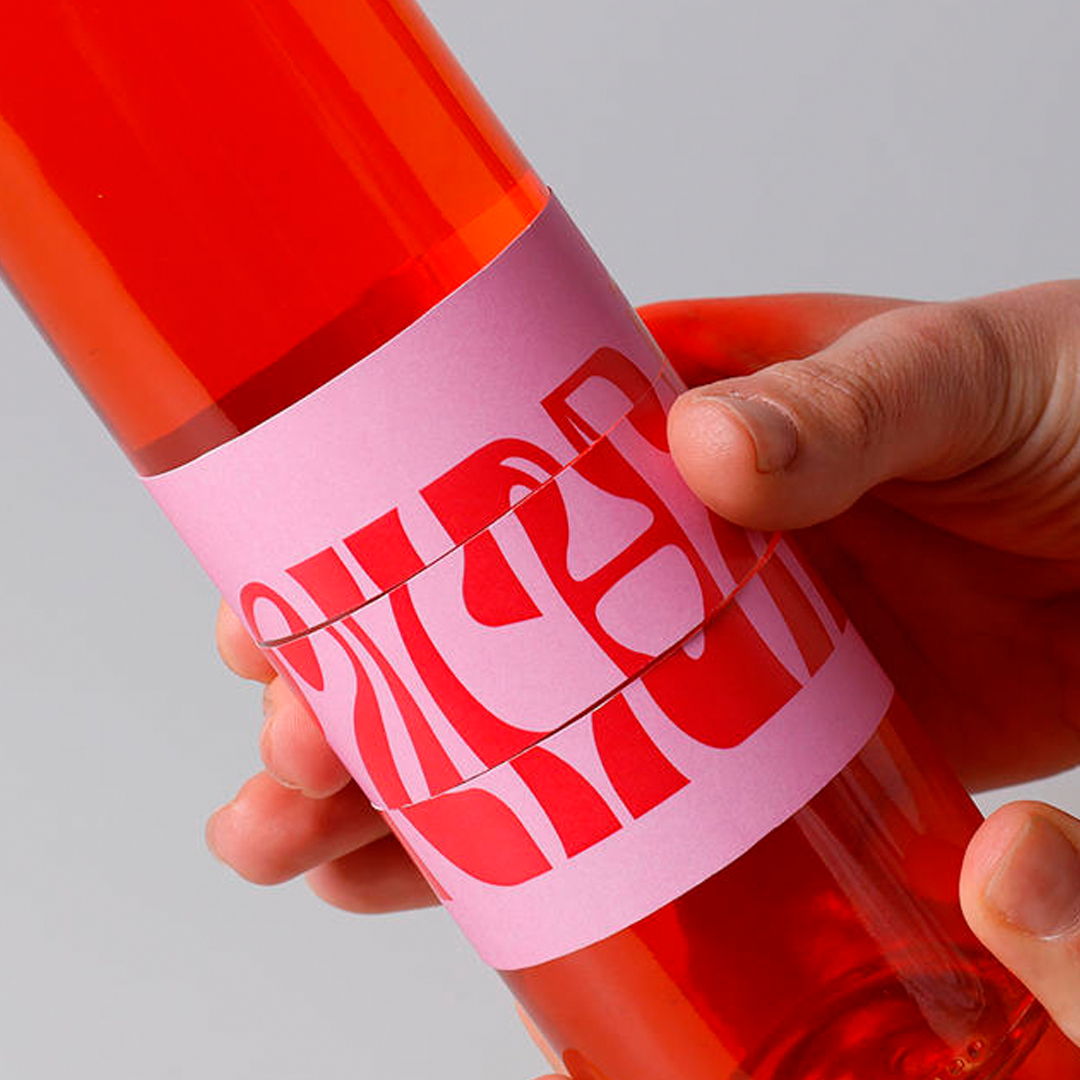 A hand holding a red bottle with a pink label design.