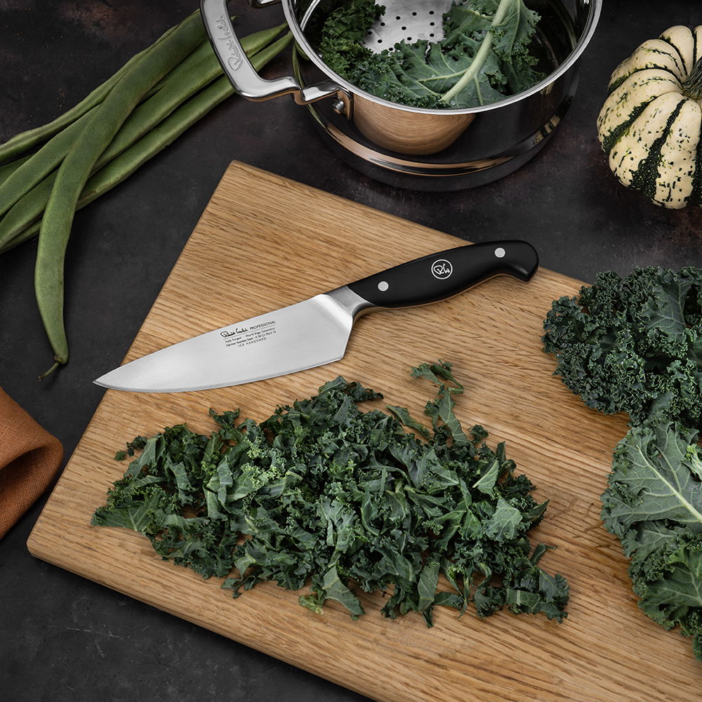 Chopped kale on a cutting board with the 15cm Professional Chef’s Knife and vegetables in the background.