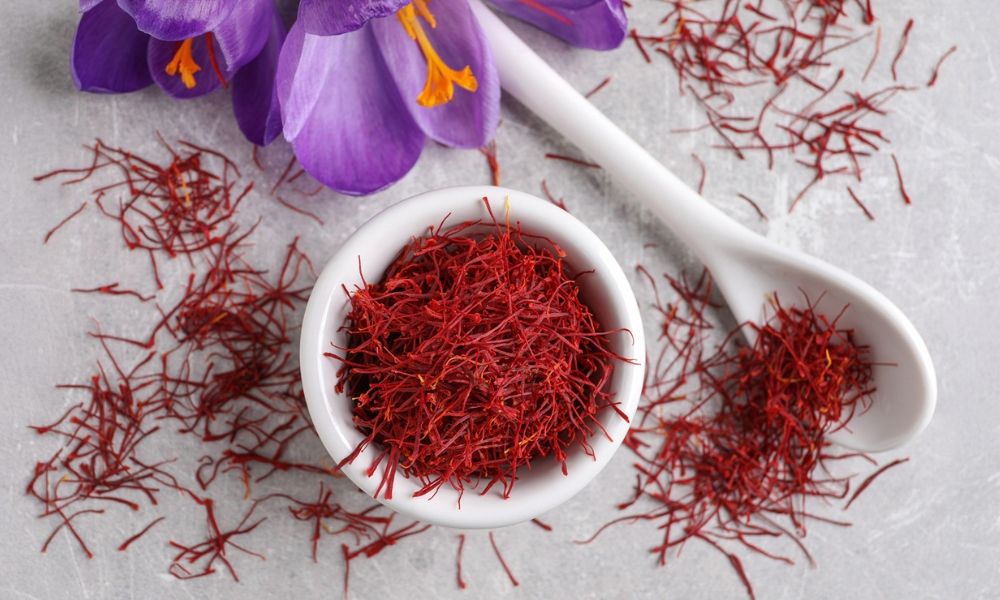 A bowl of saffron threads with a purple flower and a spoon.