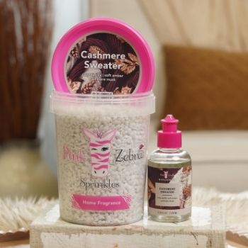 Container of cashmere sweater fragrance beads and oil on a decorative surface.