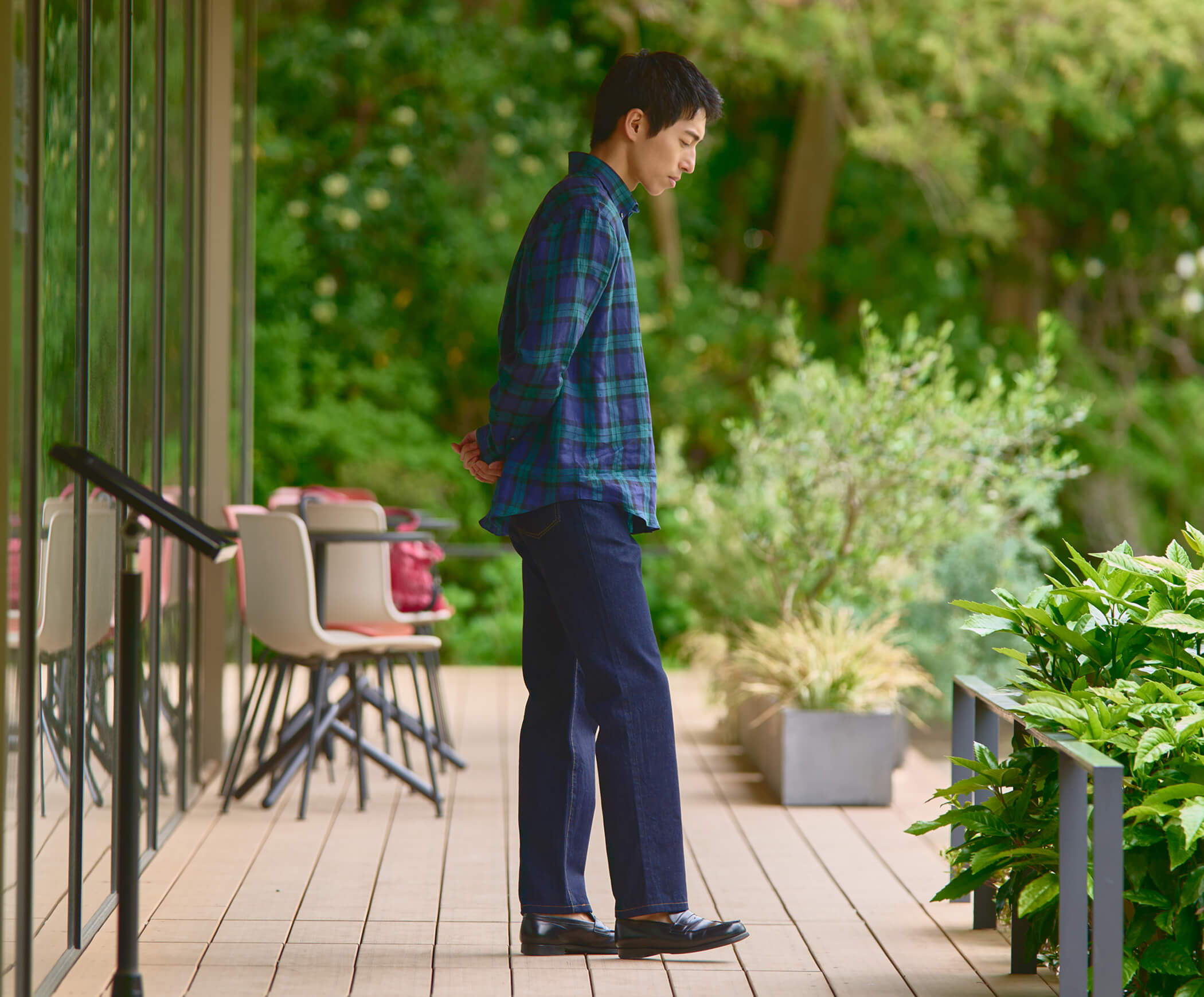 Person standing on a deck surrounded by greenery, lost in thought.