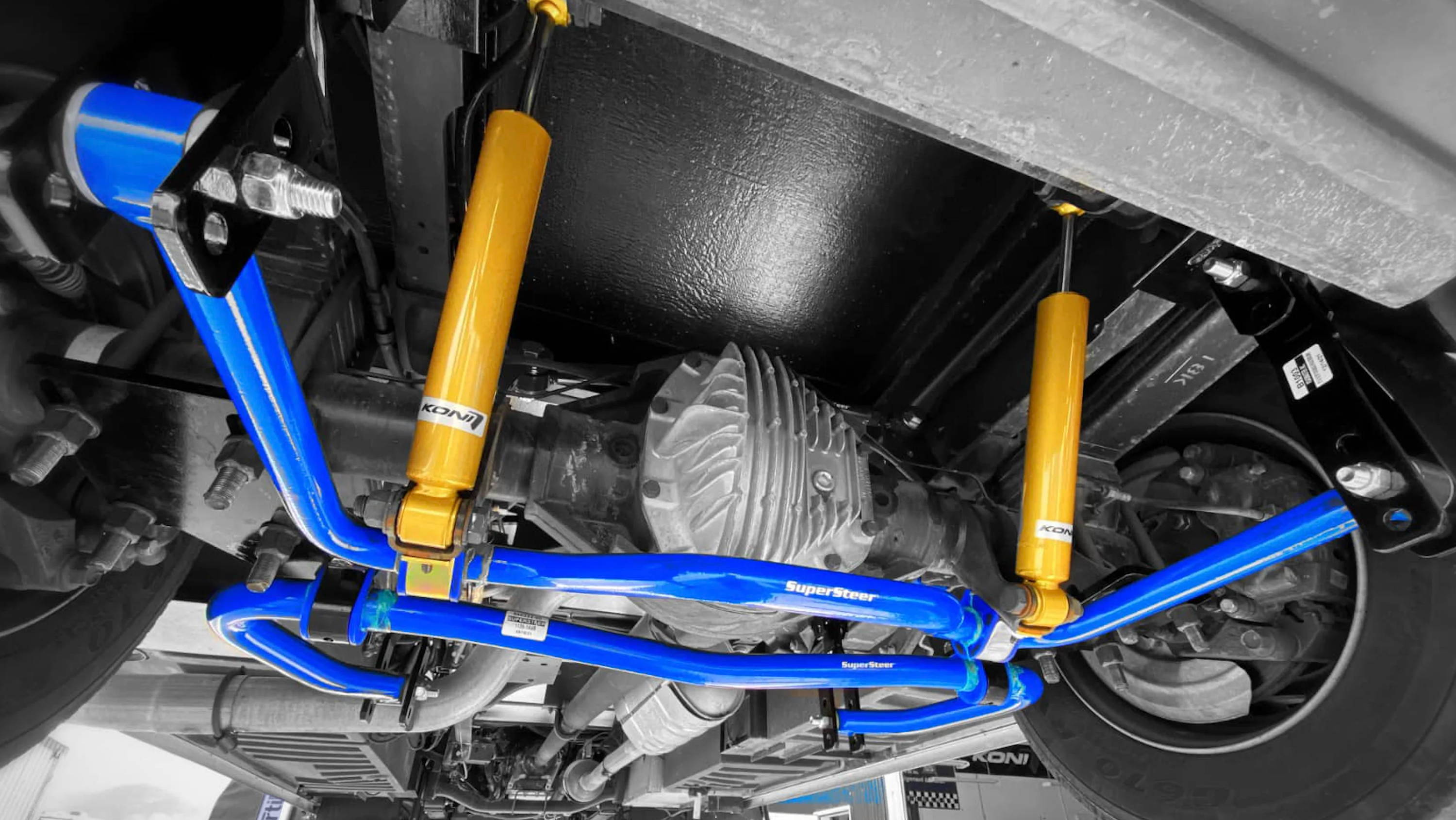 Suspension components with blue and yellow parts viewed from underneath a vehicle.