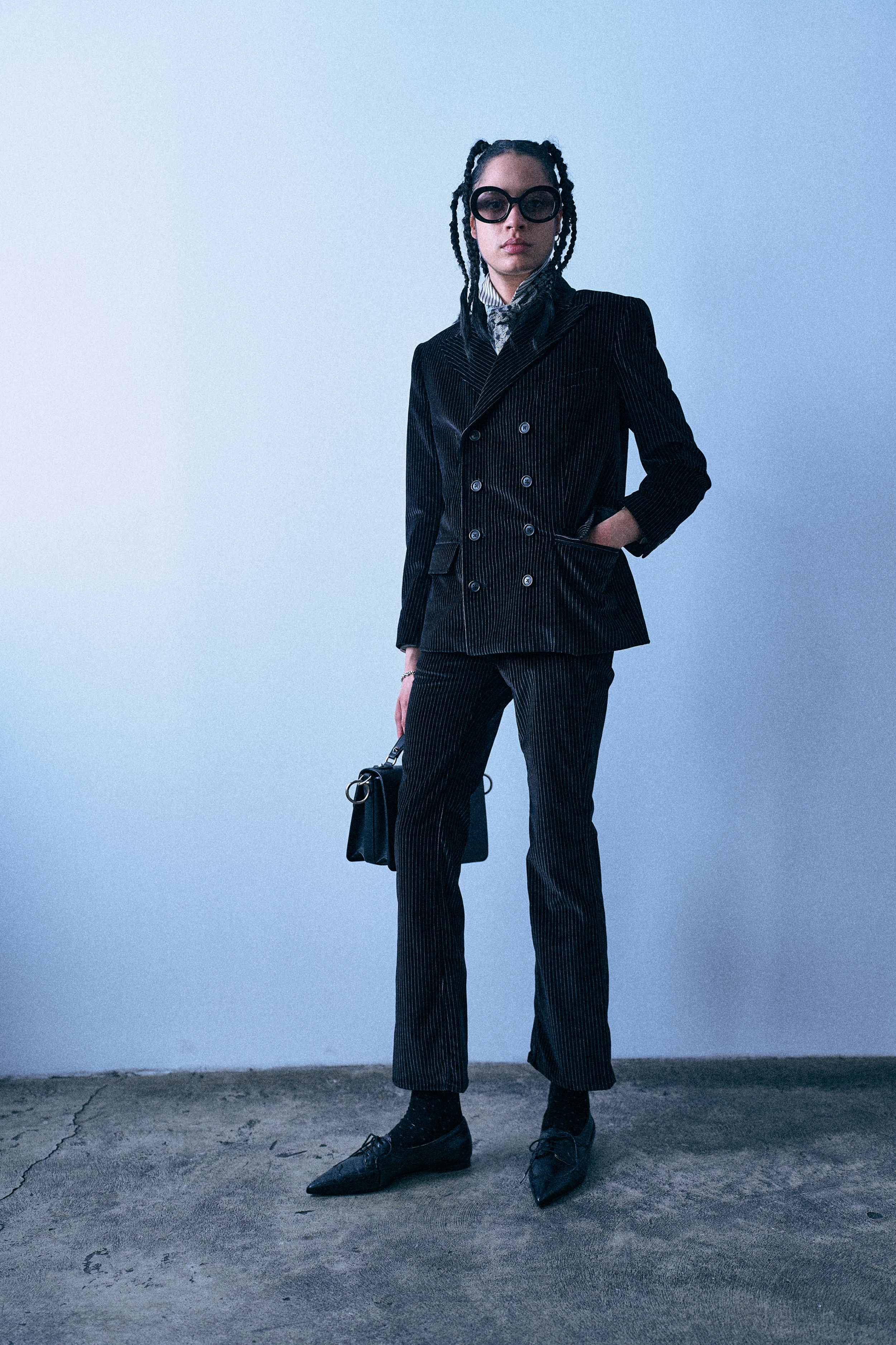 Person in a stylish black suit and sunglasses, standing against a plain background.