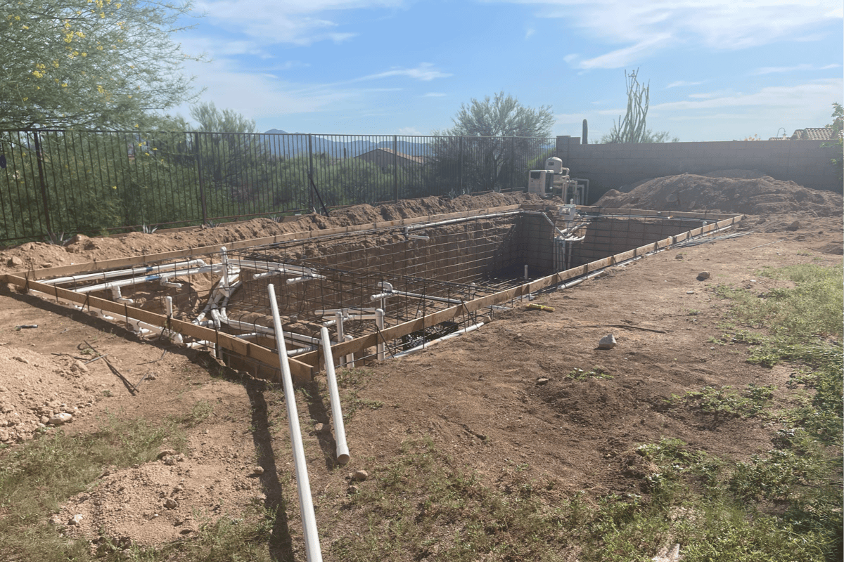 Pool construction site with rebar, plumbing lines, and a formed pool shell in a backyard, before concrete and hardscape are poured.