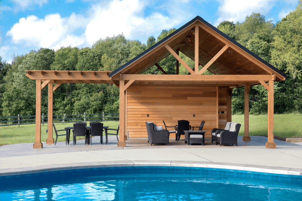Poolside pavilion with a wood outdoor structure, woven dining chairs, cushioned lounge seating, and a covered patio arranged beside a swimming pool.