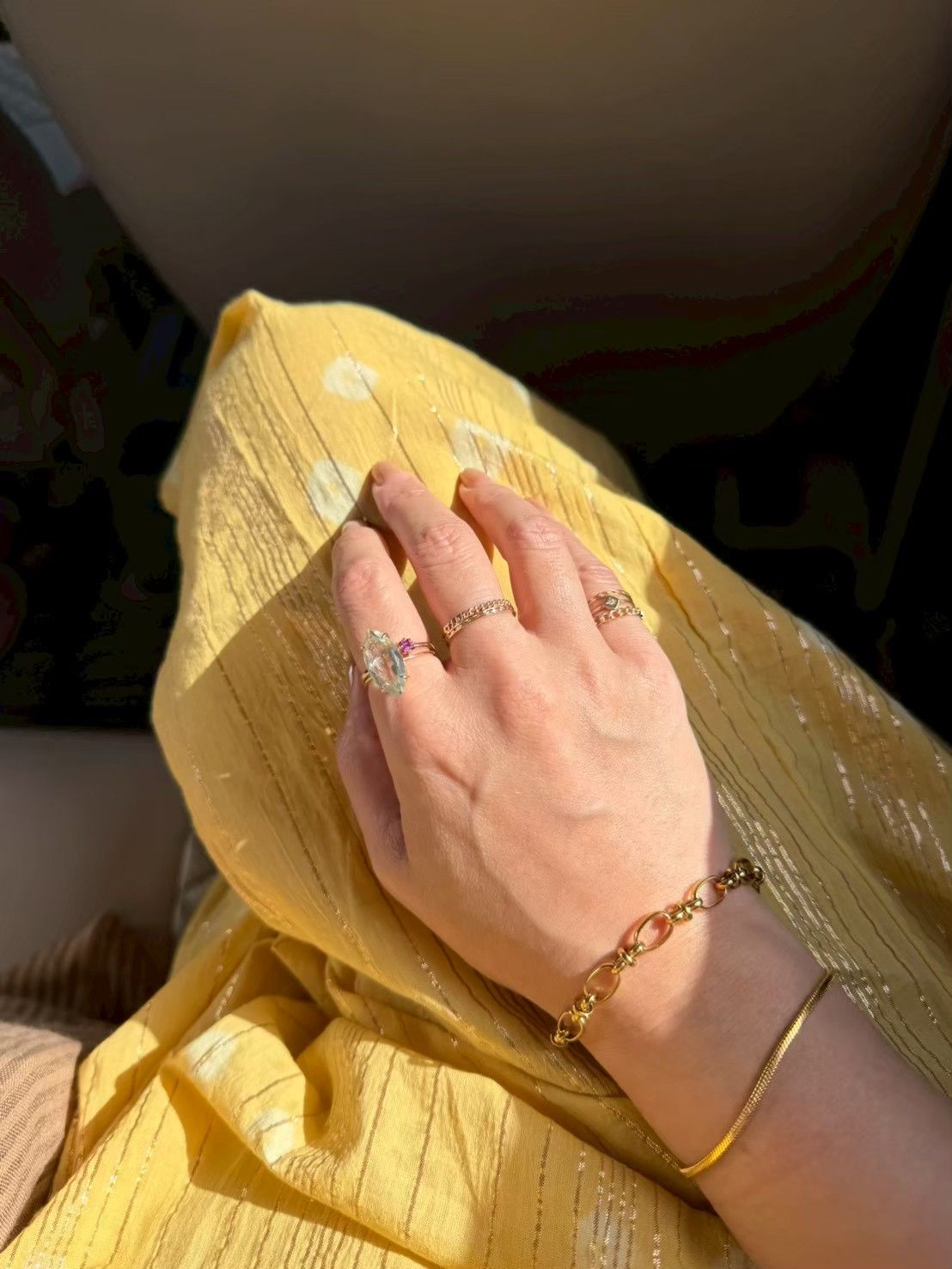 A hand adorned with rings resting on a bright yellow fabric.