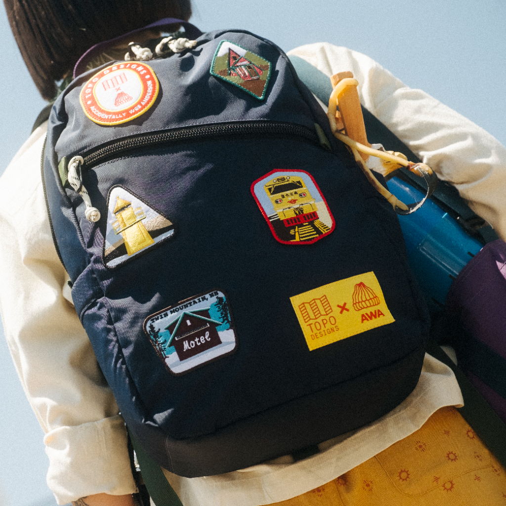 Person wearing a backpack adorned with various colorful patches and stickers.