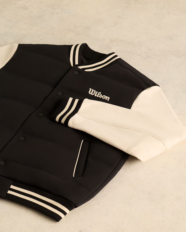 Black and white varsity jacket with Wilson logo, laid on a flat surface.