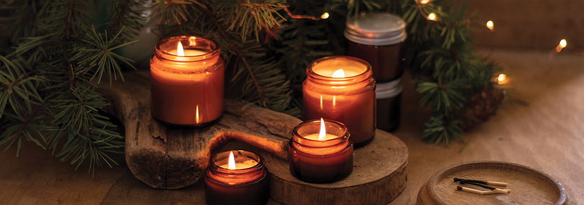 Four lit candles arranged on a wooden surface with greenery and soft lighting.